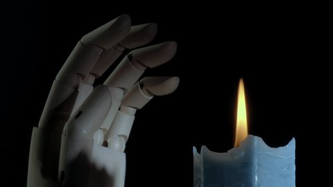 Closeup shot of a burning candle rotating and a creepy mannequin hand. Creepy candlelight. Religion concept. Dark blue candle. Studio shot. Black background.