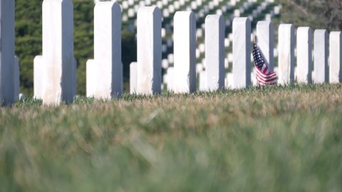 Tombstones and american flag, national memorial cemetery, military graveyard in USA. Headstones or gravestones, green grass. Respect and honor for armed forces soldiers. Veterans and Remembrance Day.