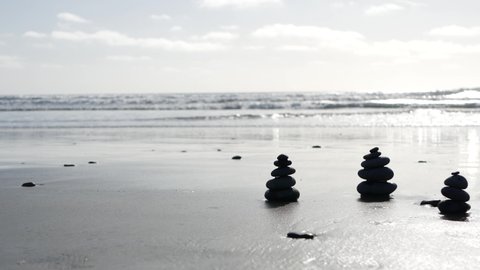 Rock balancing on ocean beach, stones stacking by sea water waves. Pyramid of pebbles on sandy shore. Stable pile or heap in soft focus with bokeh, close up. Zen balance. Seamless looped cinemagraph