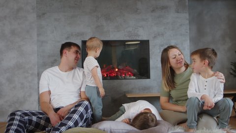 Happy affectionate parents and little children sons together cudding, feeling love bonding sitting near fireplace in cozy home indoors. Enjoy calm family leisure, carefree quiet relax, tender embrace