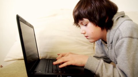 Young boy lying on sofa with laptop