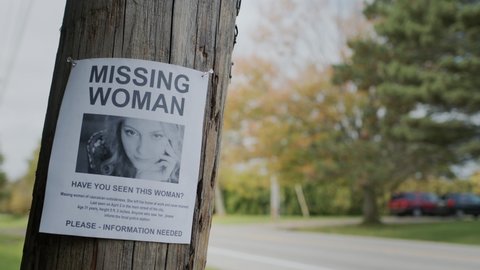An advertisement for a missing young woman hangs on a pole near the road
