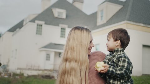 Portrait of a happy mother with a baby in her arms against the background of a large house