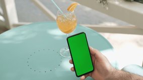 View of female hand holding and pressing on smartphone with mockup green screen in the restaurant european city. Concept of chroma key and greenscreen