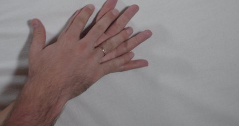 A close-up of the hands of an unrecognizable man and woman making love on a white sheet. Romance and humiliation concept