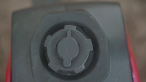 A person unscrews the gas tank cap of an inverter generator to pour gasoline. Close-up