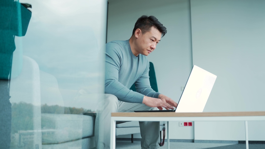 Asian male freelancer working on laptop in modern office coworking center Man student or teacher typing on computer smart professional employee creative, innovative entrepreneur co-working glass space | Shutterstock HD Video #1083133912