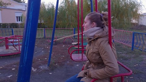Young mother on the playground sitting on a swing