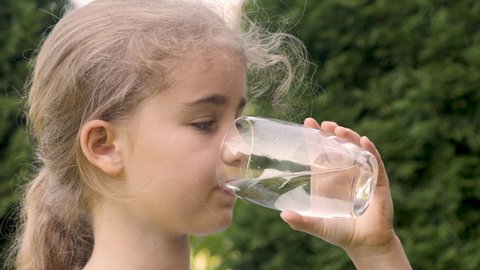 Thirsty Child Drinking Water From Glass Outdoors With Sun Shining. Cute Girl Drinking Glass Fresh Transparent Pure Filtered Water Slow Motion Kid Drinking Cup Water Healthy Body Care Healthy lifestyle
