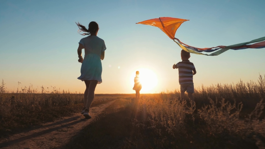 Happy young mother with a children play kites together on park. Boy running with flying kite in hand. Silhouette of happy people running at sunset in the park. Happy parents childhood dream concept. Royalty-Free Stock Footage #1083144001