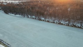 Festive winter landscape with frozen river at sunset, aerial view. The ground is covered with white snow. Video, footage, splash screen, intro, presentation, copy space. UHD 4K.