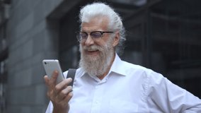 Mature oldster laughing watching funny videos on smartphone, waiting bus or taxi