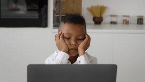 Closeup portrait of bored little black boy looking at laptop screen while sitting at desk at home, tired african american child resting head on hands while watching video on computer, slow motion - Powered by Shutterstock - Get 15% off with code: PIKWIZARD15