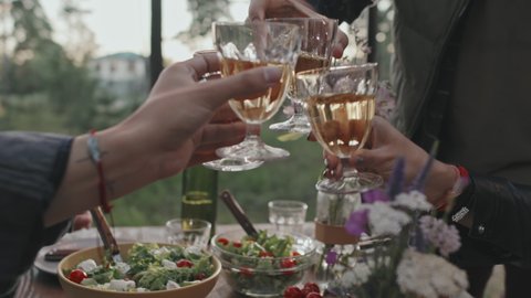 Close up mid-section of friends having picnic outside on summer evening and clinking glasses. People enjoying dinner outdoors
