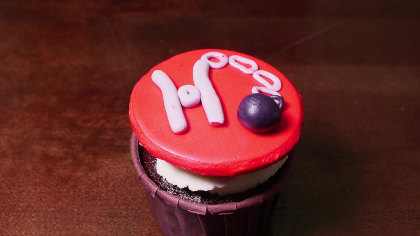 Close up view of cupcake with miniature of nipple clamp on it as a decoration. Man hand takes it and removes it from table.