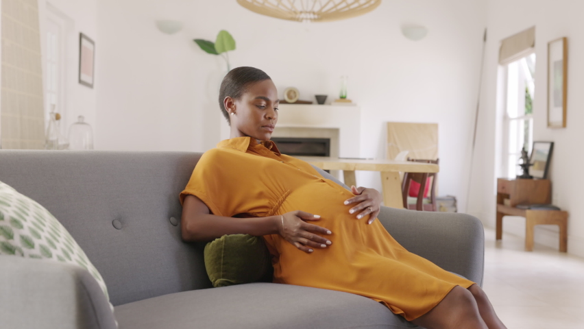 Mature pregnant woman having a backache at home. Unhappy black expecting woman suffering from lower back pain on last month of pregnancy sitting on sofa with copy space. Tired mid adult pregnant woman