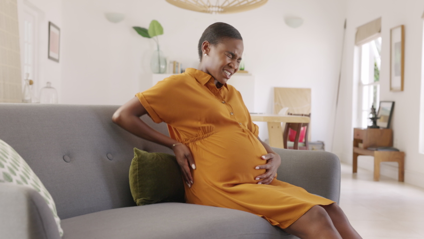 Mature pregnant woman having a backache at home. Unhappy black expecting woman suffering from lower back pain on last month of pregnancy sitting on sofa with copy space. Tired mid adult pregnant woman | Shutterstock HD Video #1083153817