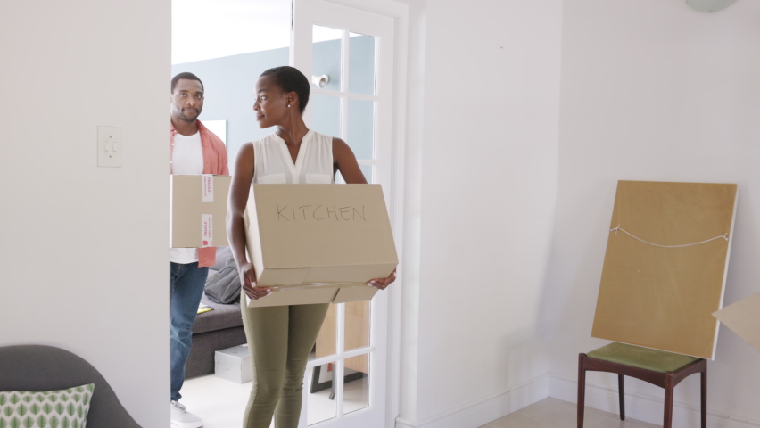 Happy african american man and woman holding cardboard boxes during moving house. Newly wed married black couple shifting home. Middle aged couple holding cardboard boxes while moving to new home. | Shutterstock HD Video #1083153823