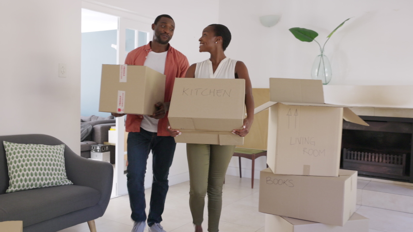 Happy african american man and woman holding cardboard boxes during moving house. Newly wed married black couple shifting home. Middle aged couple holding cardboard boxes while moving to new home.