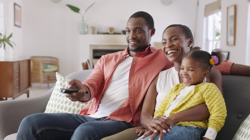 African american family watching TV together. Happy mature father changing television channel using remote control with daughter sitting on mother's lap at home. Black family watching movie together. | Shutterstock HD Video #1083153844