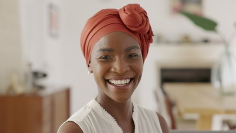 Portrait of smiling middle aged woman with headscarf at home. Cheerful mid adult black woman with turban looking at camera. Happy mid mature lady wearing traditional african scarf on head.