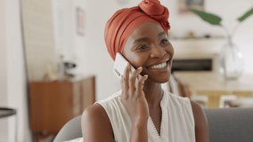 Smiling middle aged woman sitting on couch talking over smartphone. Happy black woman with traditional head turban using mobile phone for conversation. Relaxing mid african american lady using phone. - Powered by Shutterstock - Get 15% off with code: PIKWIZARD15
