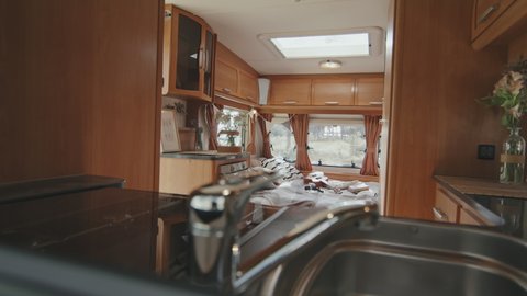 Tracking shot of interior of cozy camper with small kitchen and bed