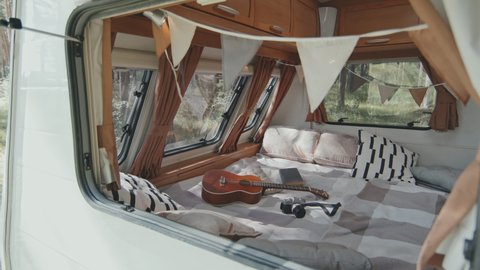 Handheld tracking of interior of cozy camper decorated with fabric flags garlands. Ukulele and digital camera lying on bed