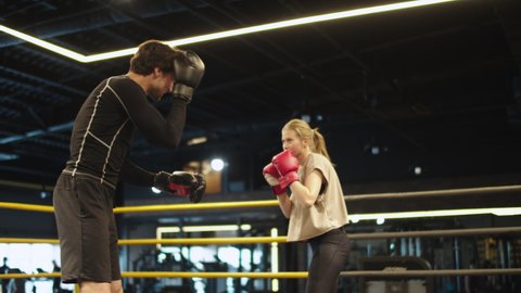 Smiling coach training with female athlete on boxing ring. Closeup attractive male and female boxers practicing hits at gym. Sporty couple boxing in sport club.