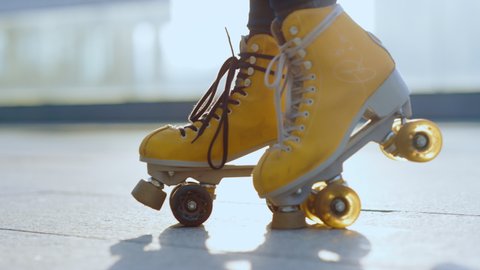 Closeup woman feet riding rollerblades against sunlight outdoor. Unknown girl staying on roller skates outside. Unrecognizable roller skater waiting for workout at city background.