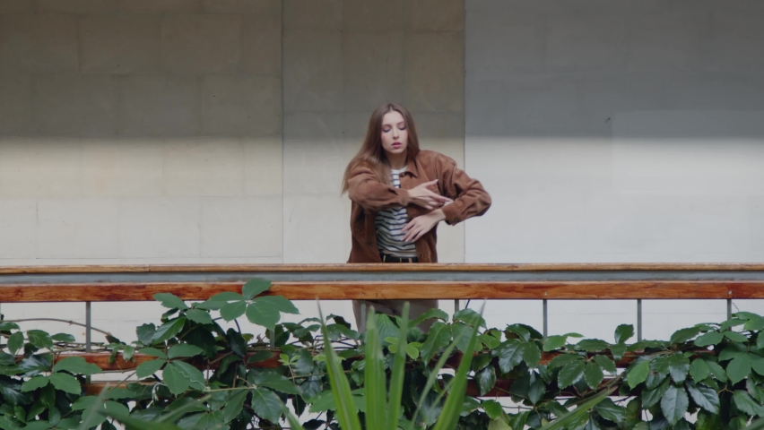 Young tender lady is dancing alone near balustrade, decorated with green plants, dancer is moving with inspiration, looking at camera, taking pleasure of favorite activity, Slow motion.