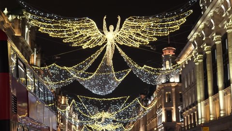Sparkling illuminated Christmas angel flying above against dark sky in London's Regent Street at night, double - decker buses driving past.