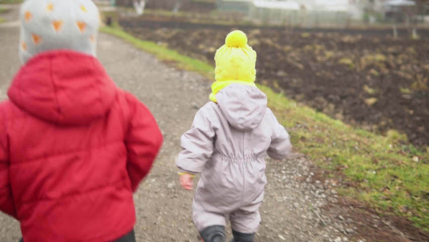 baby running. Two little kids in grey jumpsuit yellow hat walking through forest park path. kid dream funny family concept. Siblings outside. fun happy childhood carefree Children boy girl walk in yard