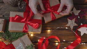 female woman hands wrapping Christmas presents gift box with brown craft paper, tying red ribbon bow on wooden desk with new year ornaments: stars light garland and green coniferous. top view DIY home - Powered by Shutterstock - Get 15% off with code: PIKWIZARD15