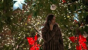 Beautiful woman talking over smartphone near christmas tree in city center