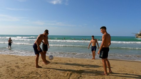 Vasto , Italy - 08 18 2021: Boys have fun playing beach football seafront at Punta Penna in Abruzzo with trabocchi in background, Italy. Slow-motion