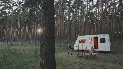 Slowmo tracking of table laden with food, grill and white camper in forest on sunny summer day