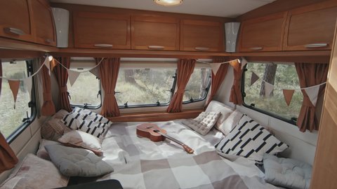 Tracking with slowmo of interior of cozy camper. Ukulele lying on bed and fabric flags garland hanging on windows