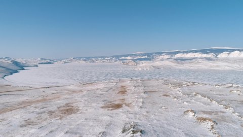 Aerial over the snow covered lands of Olkhon island in lake Baikal against the blue sky. Winter landscape of the lake Baikal.
