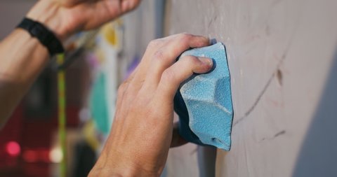 A young man of European appearance climbs up the artificial surface of the climbing wall, grabbing the artificial colored stones on the wall with his hands. Close-up of a hand