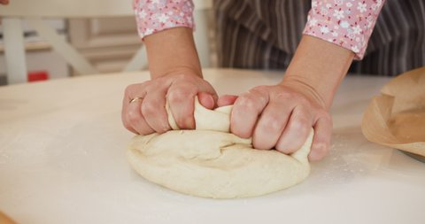 Close up female hands making dough on kitchen table. Woman baker preparing dough for homemade baked goods in kitchen