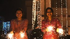 Two beautiful young Indian girls celebrating Diwali. Girls playing with fire crackers in Indian on Diwali night. Happy Indian faces on Diwali. Indian girls smiling, looking into the camera  4K - Powered by Shutterstock - Get 15% off with code: PIKWIZARD15