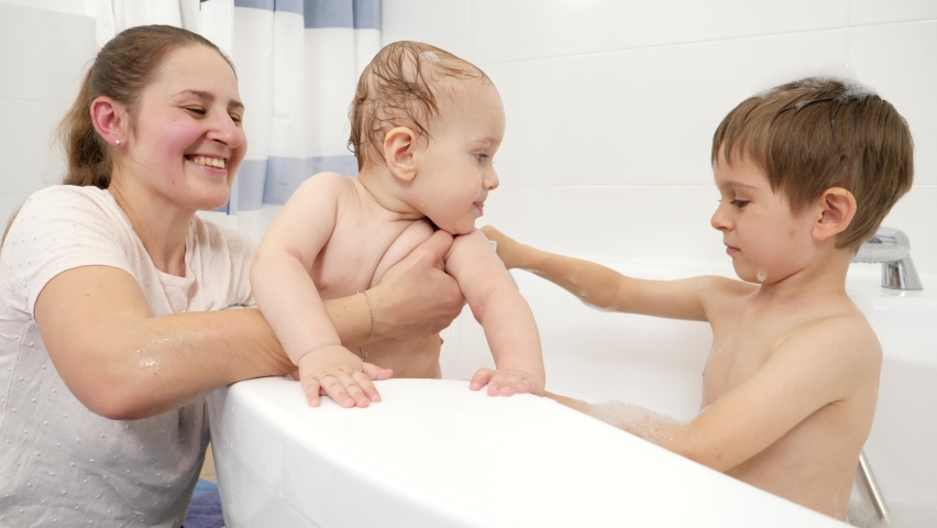Happy smiling mother and older son washing baby brother in bath. Concept of children hygiene, healthcare and family care at home
