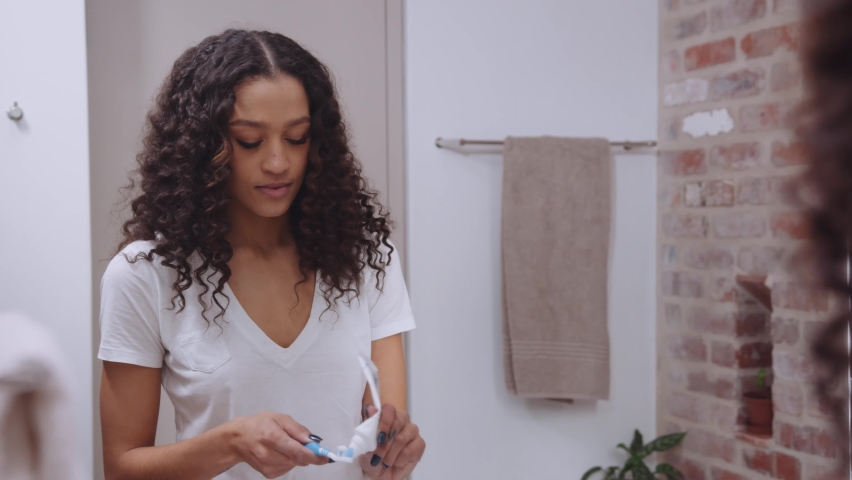 African American young female smiling whilst brushing teeth before bed looking at the mirror in a modern bathroom Royalty-Free Stock Footage #1083191326