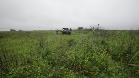 Summer, 2018 - Amursk, Khabarovsk Territory - Installation and assembly of a metal support for placing an artificial nest of a Far Eastern stork. A welder works in a field in the rain. Overall plan.
