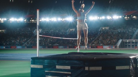 High Jump Championship: Professional Female Athlete Running, Successfully Jumping over Bar. Happy Sportswoman Celebrates Winning with Stadium Full of Spectators Cheering. Cinematic, Slow Motion