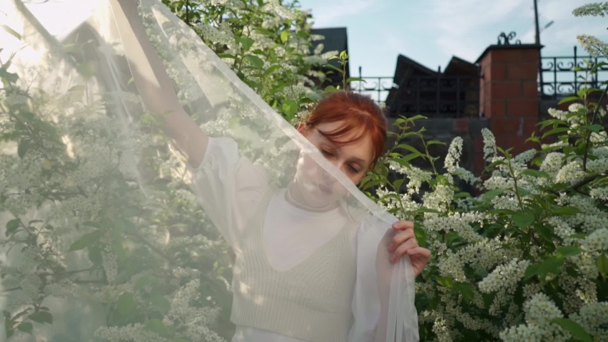 A young girl in a white dress against the background of greenery and sun. Day in the park. Ginger girl