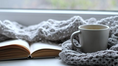 Cozy home with cup of coffee and a book. Hygge style. Mug of black coffee wrapped in warm scarf on wooden board. Top view, vintage style, Still life.