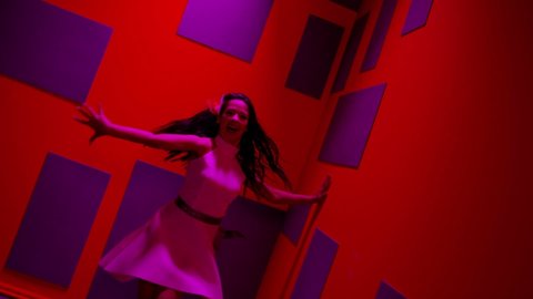 Beautiful girl dressed in white dress dancing , moving , smiling  inside decorated pavilion  with purple cubes and red  wall background  Female dancer with black hair showing stylish dress and dances