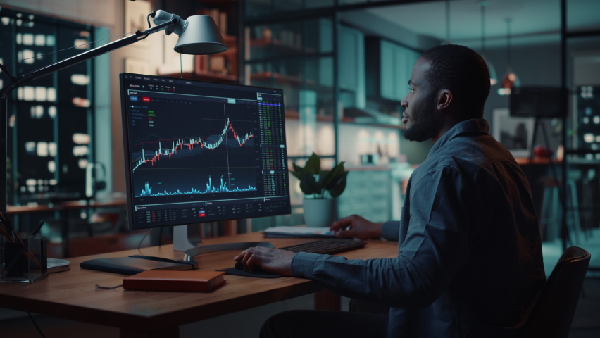 Home Office Evening: Black Financial Analyst Using Computer with Display Showing Real-Time Stocks, Exchange Market Charts. Remote Working African American Trader making e-Commerce Investment Royalty-Free Stock Footage #1083198973